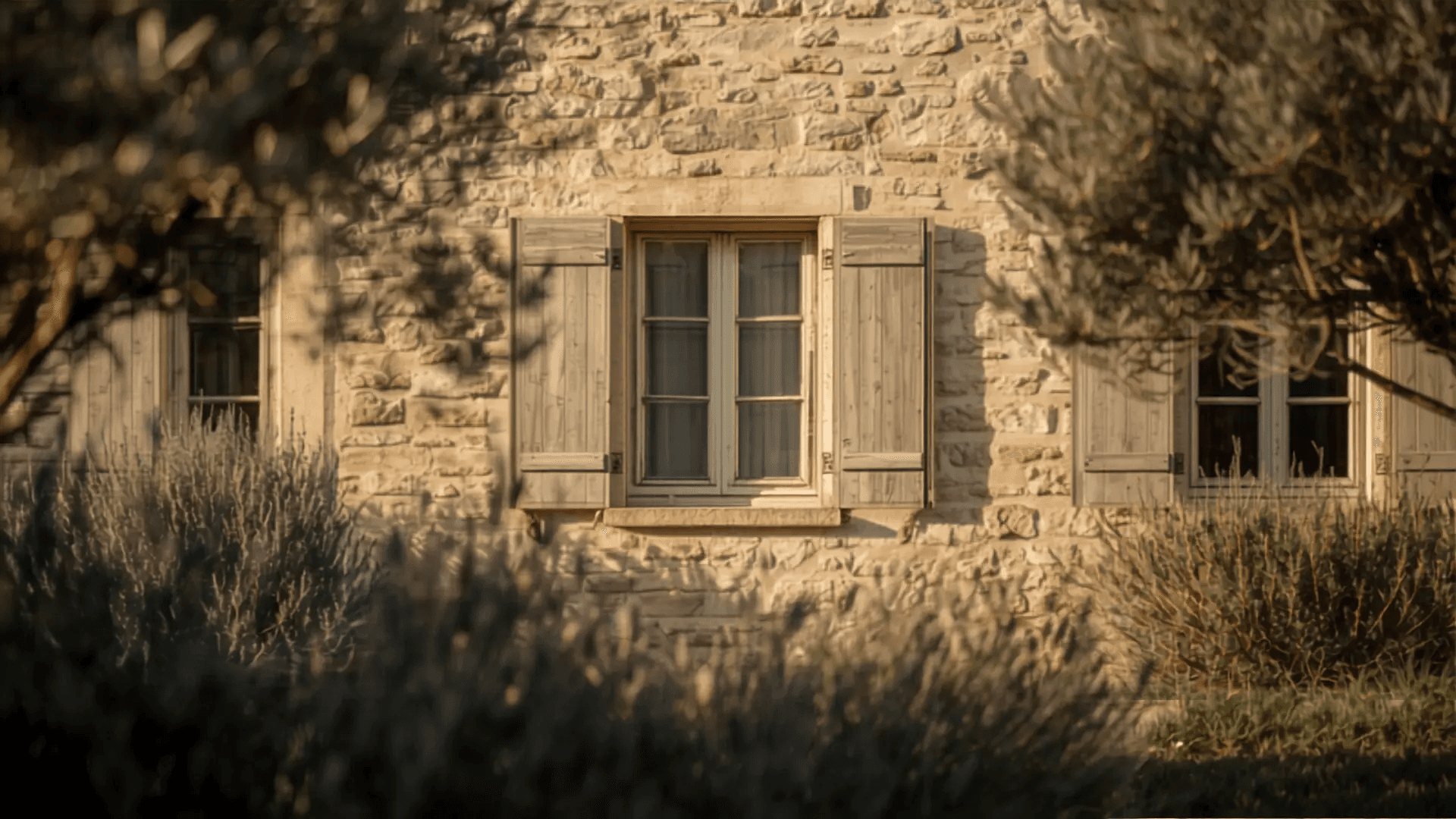 Façade d'une villa provençale en pierre avec volets fermés, boîte aux lettres et jardin d'oliviers en fin d'été